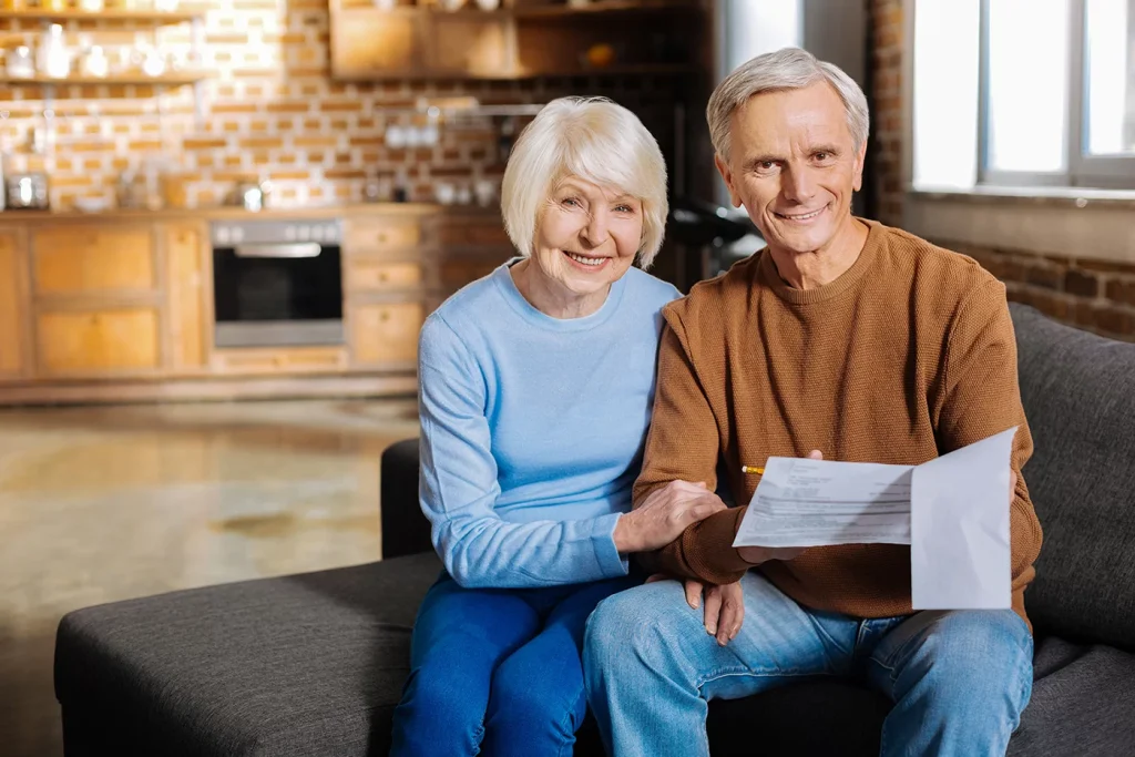 Smiling senior couple sitting on a couch, reviewing SSDI documents in a cozy home environment.