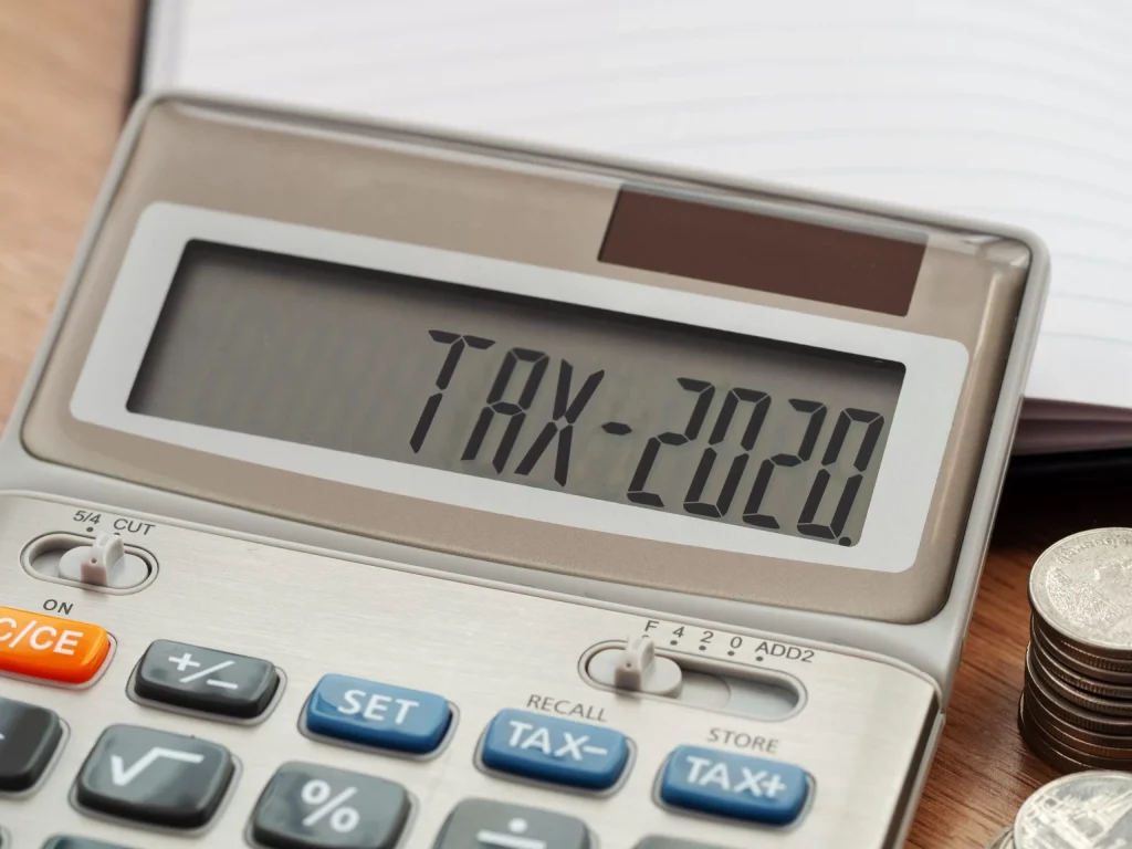 Close-up of calculator displaying TAX-2020 beside coins, symbolizing tax debt and financial obligations.