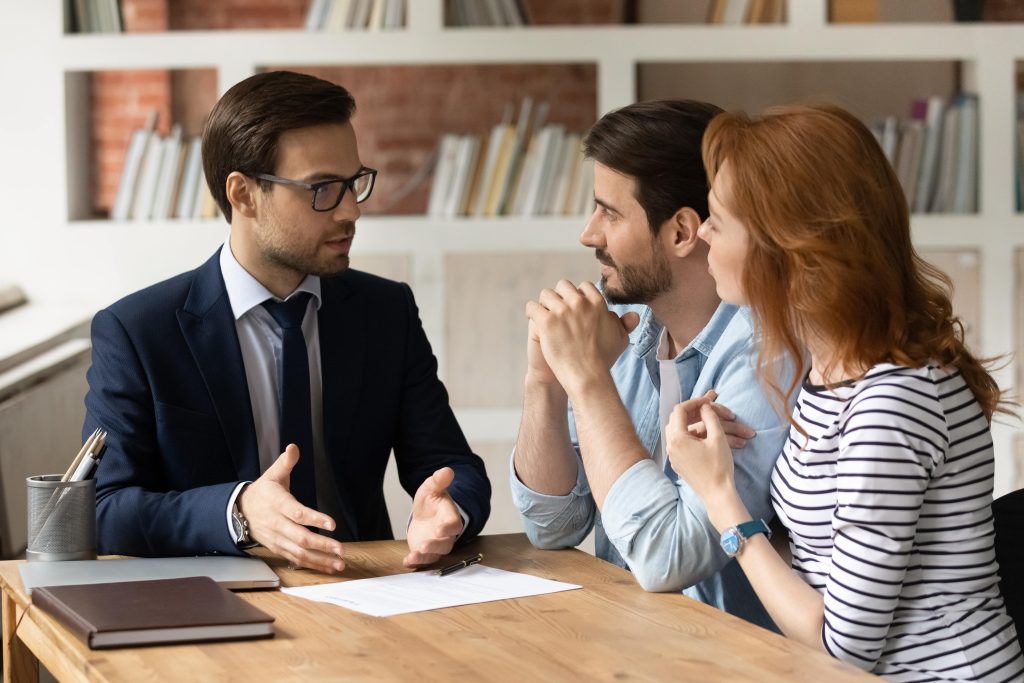 Lawyer advising a young couple during legal consultation at a wooden office table.
