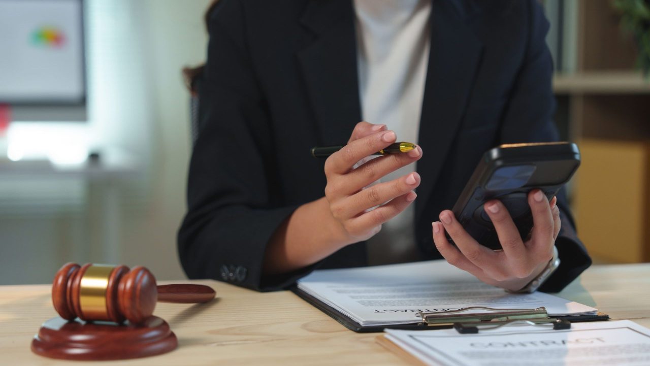 Female attorney reviewing legal documents while holding a phone and pen at her office desk