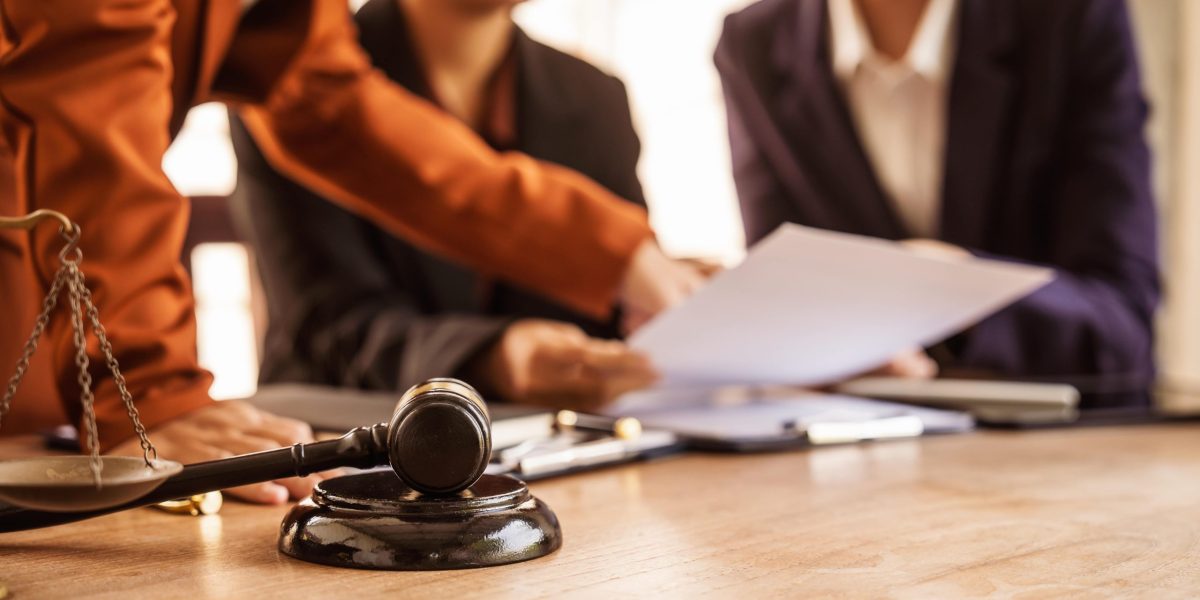 Attorney preparing legal documents in a courtroom with judges and legal professionals in session.