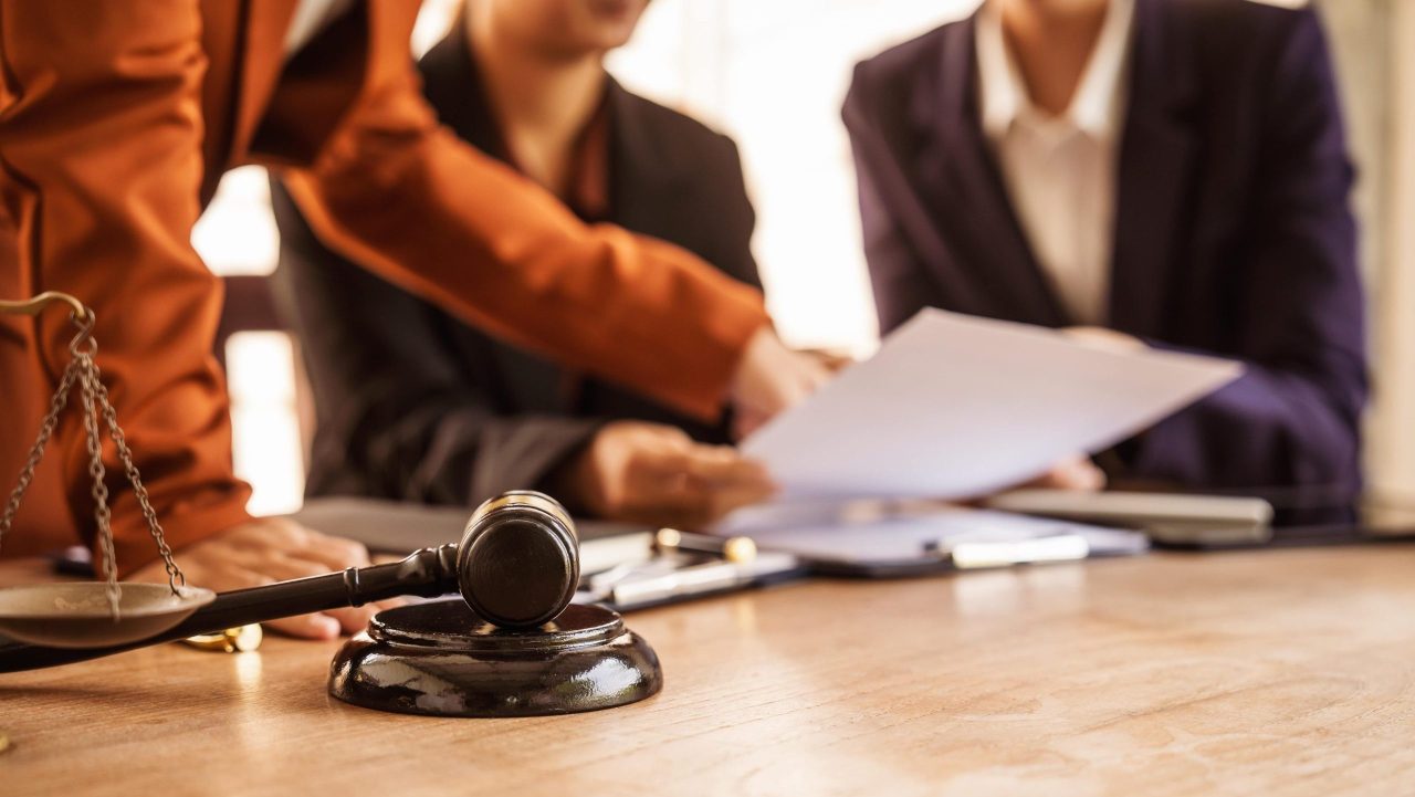 Attorney preparing legal documents in a courtroom with judges and legal professionals in session.