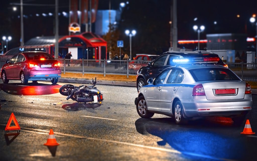 Motorcycle accident scene at night with emergency vehicles and multiple cars involved