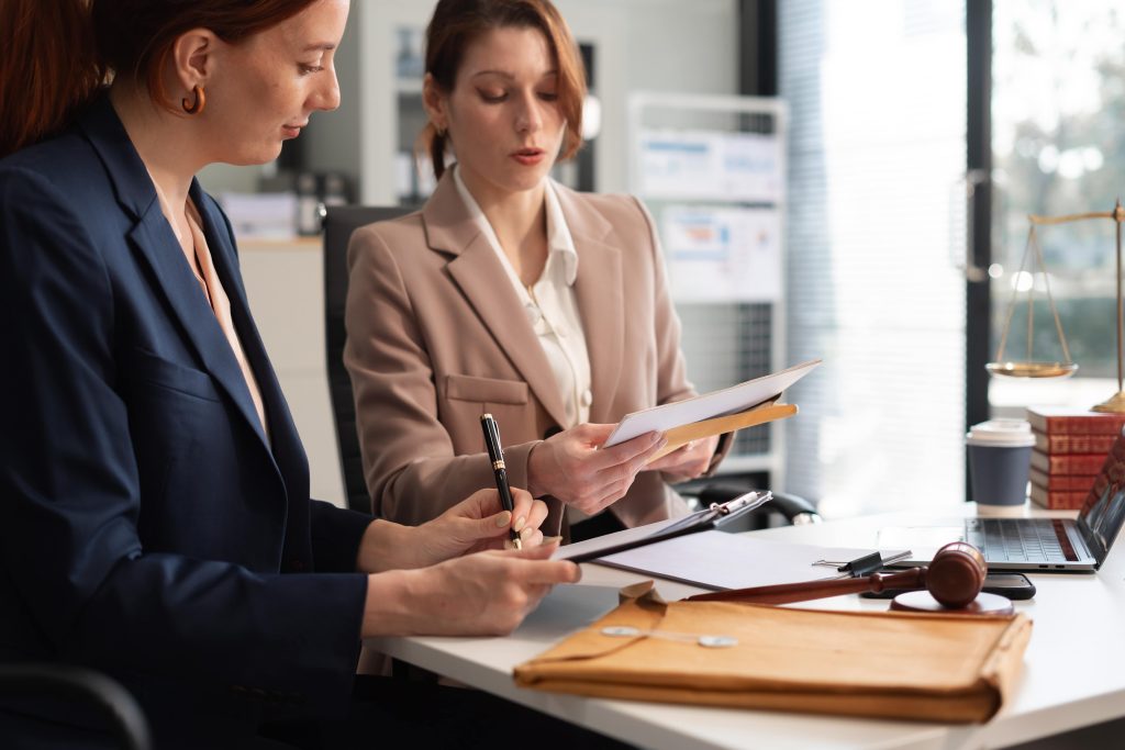 Two female legal professionals in a modern office reviewing case documents and employment law files.