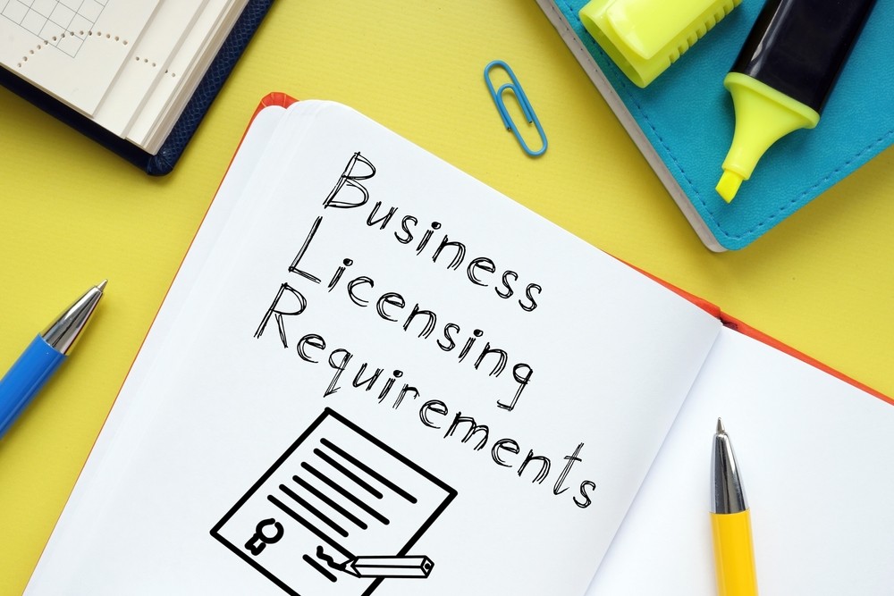 Notebook with handwritten text “Business Licensing Requirements” surrounded by office supplies