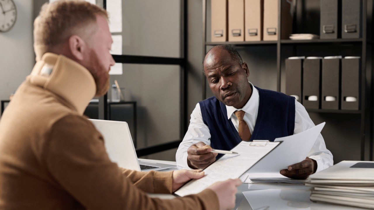 Injured man with neck brace reviewing documents with attorney